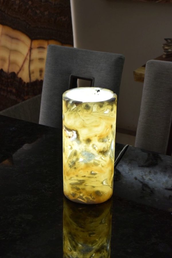 Small-sized cylindrical onyx table lamp made from Picado stone collection standing on the dinner table with lights on.