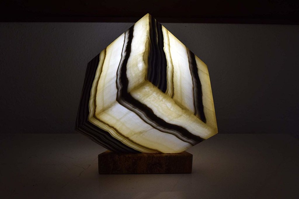Black and yellow cube table lamp made of onyx Galactea stone is standing on the nightstand with the light on