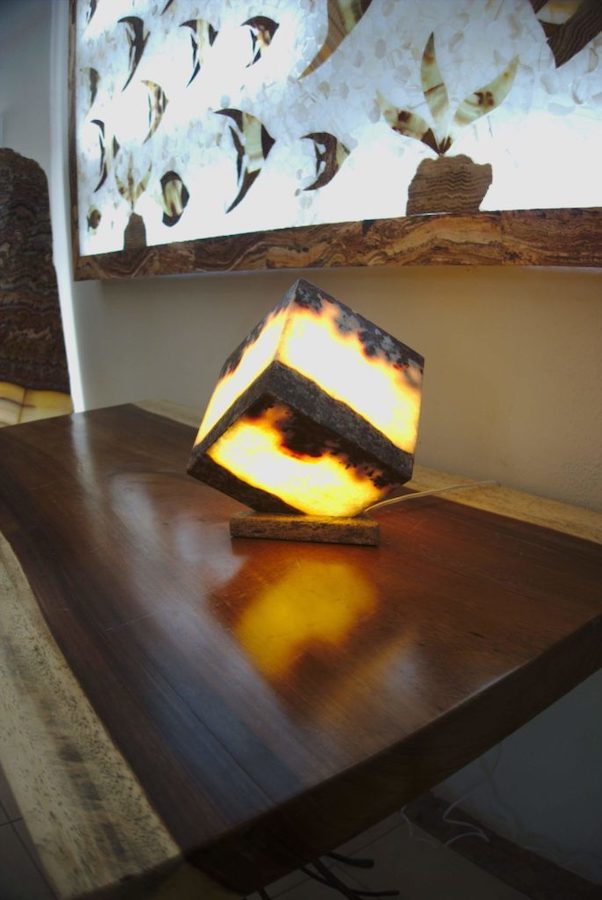Black and yellow cube table lamp made of onyx Vino stone is standing on the nightstand with light on