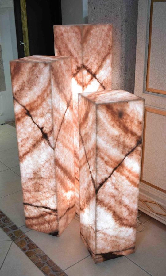 Three rectangular onyx floor lamps with closed top made from onyx rosa cristal collection with main colors being red, white, and dark brown.