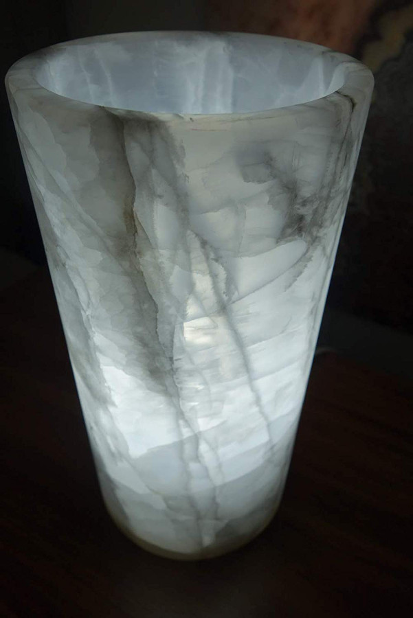 Close up shot of the cylindrical onyx table lamp made of Blanco Hielo stone collection. Main colors of the lamp are white and gray