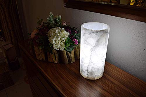 Cylindrical onyx table lamp with open top made from Blanco Hielo stone collection standing next to the mirror