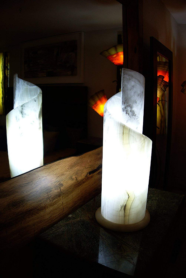 Spiral onyx table lamp made from Blanco Hielo stone standing in the dark next to the mirror with light on